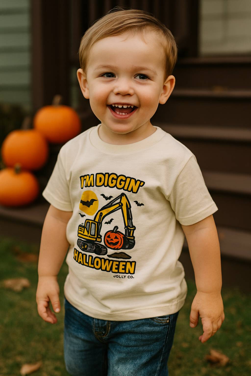 Child wearing a Halloween-themed t-shirt with pumpkins and an excavator graphic, standing outdoors with pumpkins in the background.