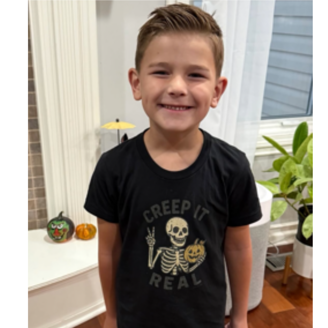 Child wearing a black t-shirt with a skeleton design in a room with Halloween decorations.