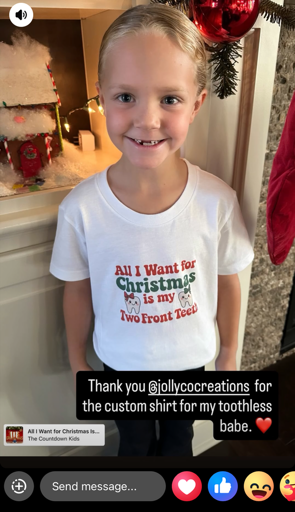 Child wearing a white t-shirt with text, standing in front of a decorated Christmas tree.